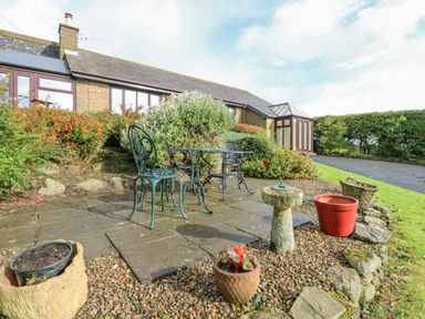 An outdoor patio area with metal table and chairs surrounded by potted plants and shrubs at Pinegarth in Catton near Allendale
