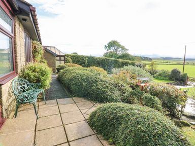 A garden area with a green metal bench next to a stone building and manicured bushes at Pinegarth in Catton near Allendale