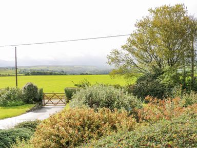 A garden with bushes and trees overlooking green fields with a wooden gate in the distance at Pinegarth Catton near Allendale
