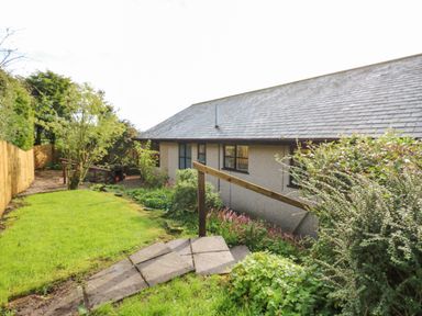 A garden with a grass lawn a path and a building with windows at Pinegarth in Catton near Allendale