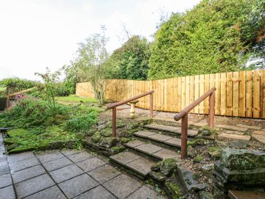 An outdoor garden area with stone steps and metal railings next to a wooden fence and greenery at Pinegarth in Catton near Allendale
