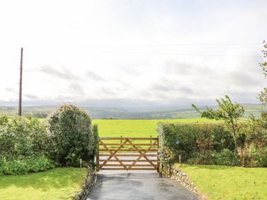 A wooden gate with green hedges and a road leading to an open green field at Pinegarth in Catton near Allendale