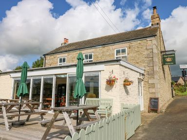 A stone building with outdoor wooden picnic tables and green umbrellas at The Crown Country Inn