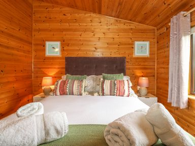 A bedroom with a bed having pillows and rolled towels on it with wooden walls and curtains at Derwent Lodge in Keswick