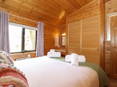 A bedroom with wooden walls and ceiling a large bed with pillows and towels a window with curtains and a wardrobe with sliding doors at Derwent Lodge Keswick