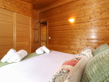 A bedroom with a bed with rolled towels and cushions and wooden walls at Derwent Lodge in Keswick