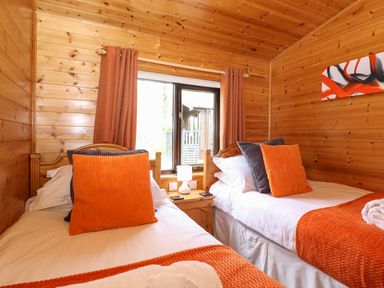 A bedroom with two single beds orange pillows and blankets wooden walls and a window with orange curtains at Derwent Lodge Keswick