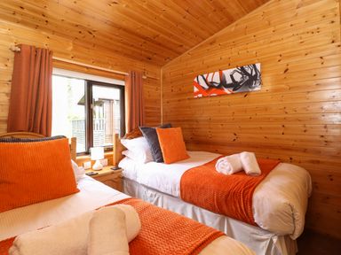 A bedroom with two single beds with orange throws and pillows and wooden walls at Derwent Lodge in Keswick