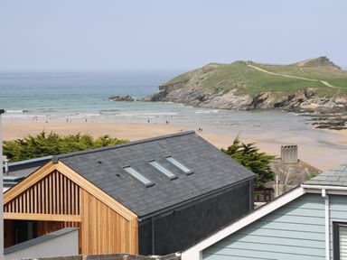 A beach with people walking near the sea and rocky green hill in the background viewed from houses at 11 Ebbtide in Porth