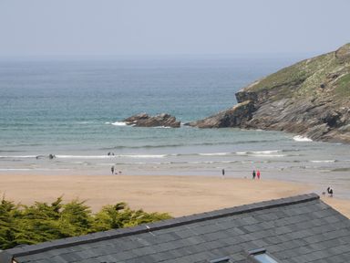 A beach with people and dogs near the ocean and rocky cliffs visible at 11 Ebbtide in Porth