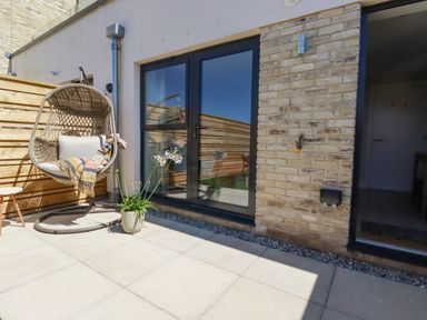 A patio with a hanging chair a potted plant and glass doors at 11 Ebbtide in Porth