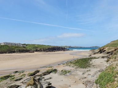 A sandy beach with rocks and seaweed with green hills and buildings in the background at 11 Ebbtide in Porth