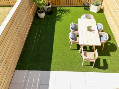 A garden patio with wooden table and six wicker chairs on artificial grass at 11 Ebbtide in Porth