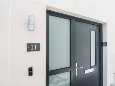 Modern black front door with frosted glass panels a wall light a doorbell and house number 11 at 11 Ebbtide in Porth
