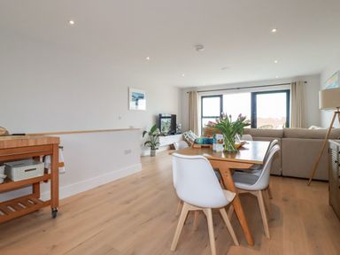A dining table with chairs and flowers in a living room with a sofa and a TV at 11 Ebbtide in Porth