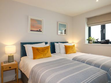 A bedroom with two single beds with yellow bird cushions and bedside tables with lamps at 11 Ebbtide in Porth