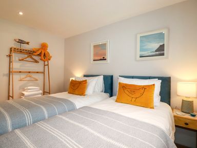 A bedroom with two single beds with yellow bird pillows and a wooden rack with hangers and stuffed toys at 11 Ebbtide in Porth