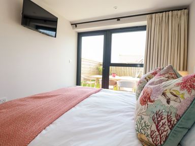 A bedroom with a bed facing glass doors and patio furniture outside at 11 Ebbtide in Porth