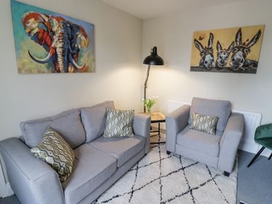 A living room with grey sofa and armchair a floor lamp and paintings of an elephant and donkeys at Dobbies Den in Bewdley