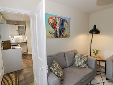 A living room with a gray sofa, patterned cushions, a floor lamp, a side table with flowers, and a colorful elephant painting on the wall at Dobbies Den in Bewdley
