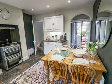 A kitchen with a wooden dining table set for four with plates glasses and flowers at Dobbies Den in Bewdley