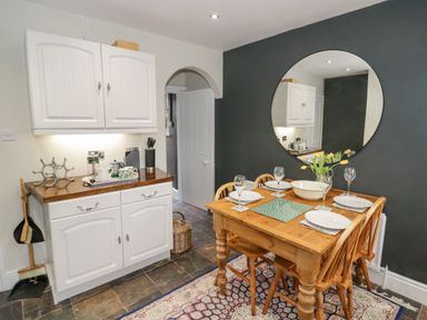 A dining area with a wooden table set for four people and a round mirror on a dark wall at Dobbies Den in Bewdley