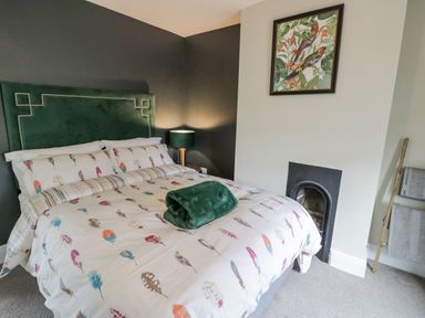 A bedroom with a bed featuring patterned bedding a green headboard bedside lamp a fireplace and a framed bird artwork at Dobbies Den in Bewdley