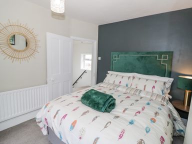 A bedroom with a bed with patterned bedding and a green headboard beside a wall with a round mirror at Dobbies Den in Bewdley