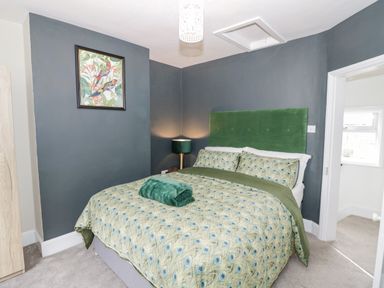 A bedroom with a bed green headboard patterned bedding and a lamp at Dobbies Den Bewdley