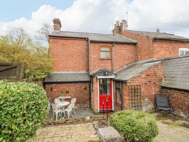 A backyard patio with white metal table and chairs and a red door on a brick house at Dobbies Den in Bewdley