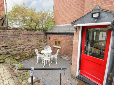 An outdoor patio with a white table and four chairs next to a red door and brick walls at Dobbies Den in Bewdley