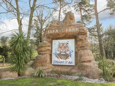 A safari park entrance sign with a lion sculpture on top and a tiger image below surrounded by trees