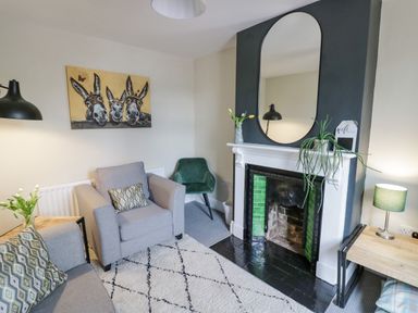 A living room with a gray armchair and sofa a fireplace with a mirror and plants and a painting of three donkeys at Dobbies Den in Bewdley