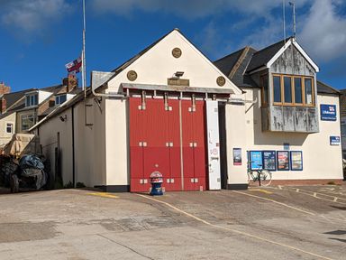 A building with red double doors and signs indicating lifeboats and a bicycle parked outside at Fairwinds in Newbiggin-By-The-Sea