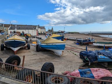 A harbor area with boats on trailers near the shore with buildings and wind turbines in the background at Fairwinds in Newbiggin-By-The-Sea
