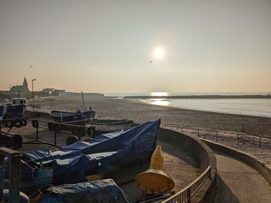 A coastal view with boats covered in tarps on the shore and a church building in the distance at Fairwinds in Newbiggin-By-The-Sea