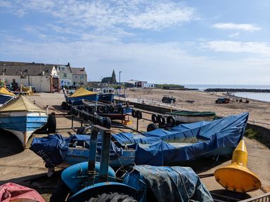 Boats and tractors on a concrete area near a sandy beach with buildings and a church in the background at Fairwinds in Newbiggin-By-The-Sea