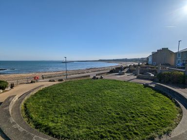 A coastal promenade with a circular grass area and a beach by the sea at Fairwinds in Newbiggin-By-The-Sea