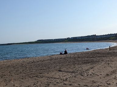 A sandy beach with people near the water and houses in the background at Fairwinds in Newbiggin-By-The-Sea