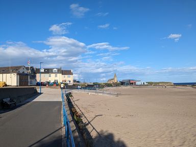 A sandy beach with a pathway and buildings including a church in the background at Fairwinds in Newbiggin-By-The-Sea