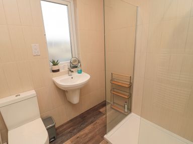 A bathroom with a toilet a sink a mirror a potted plant a soap dispenser a glass shower enclosure and wooden flooring at Fairwinds in Newbiggin-By-The-Sea