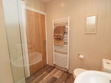 A bathroom with a wooden door a white towel radiator with towels a wall mirror toilet and washbasin at Fairwinds in Newbiggin-By-The-Sea