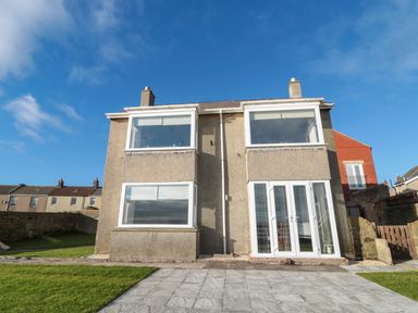 The exterior of a two-story house with large windows and a paved patio at Fairwinds in Newbiggin-By-The-Sea