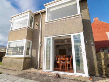 Back exterior of a house with open glass doors leading to a dining area at Fairwinds in Newbiggin-By-The-Sea