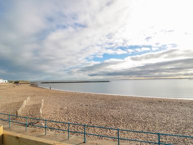 A sandy beach with a blue railing and a calm sea at Fairwinds in Newbiggin-By-The-Sea