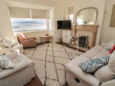 A living room with beige sofas a patterned rug a wooden fireplace and a television by Fairwinds in Newbiggin-By-The-Sea