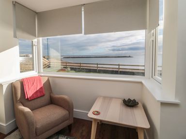 A corner with a armchair and wooden table near windows overlooking the sea at Fairwinds in Newbiggin-By-The-Sea