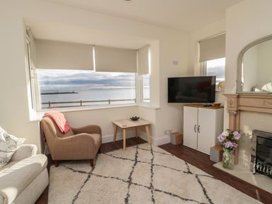 A living room with armchairs a window overlooking the sea a TV cabinet and a fireplace at Fairwinds in Newbiggin-By-The-Sea
