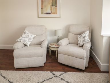 Two beige armchairs with patterned cushions and a small round table with a lamp between them at Fairwinds in Newbiggin-By-The-Sea