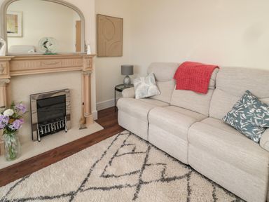 A living room with a beige sofa a fireplace with mirror above and a patterned rug at Fairwinds in Newbiggin-By-The-Sea